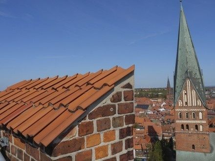 Historische Backsteinkirche mit hohem grünem Turm über einer roten Ziegeldachlandschaft